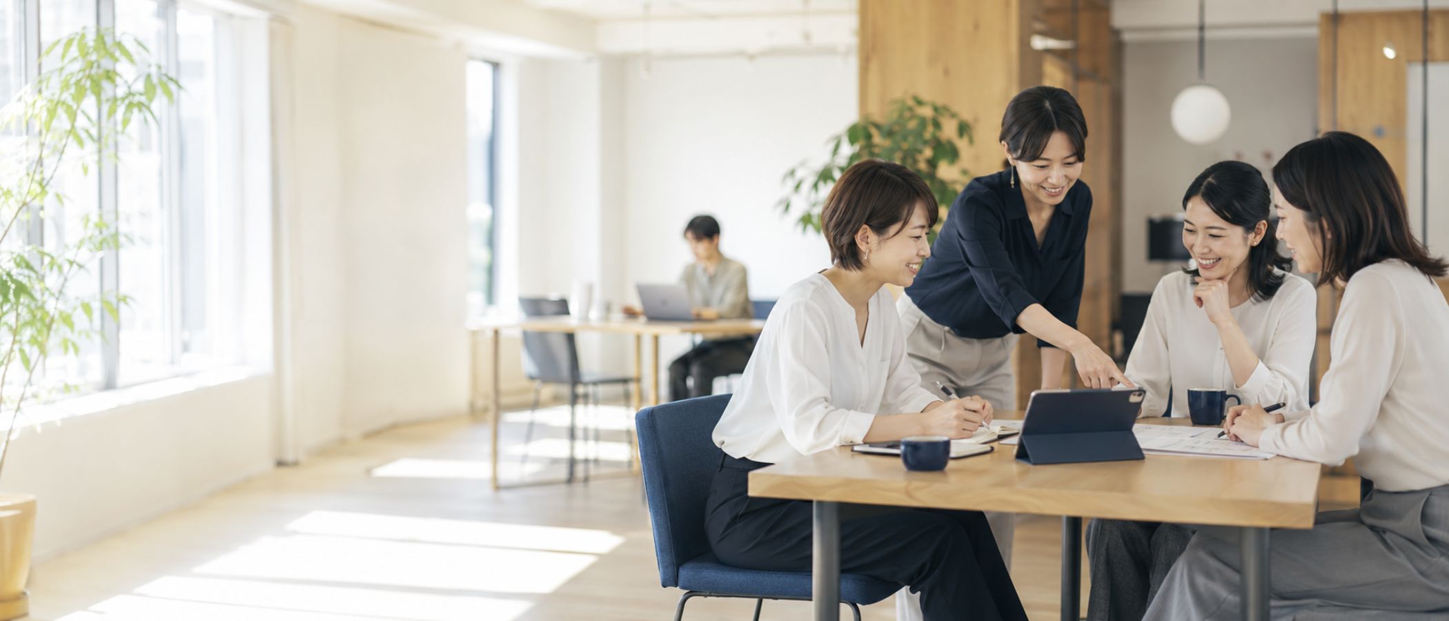 窓辺のやわらかな自然光に包まれたオフィスで、ノートとPCとグリーンが整えられた事務派遣比較サイトのメインビジュアル